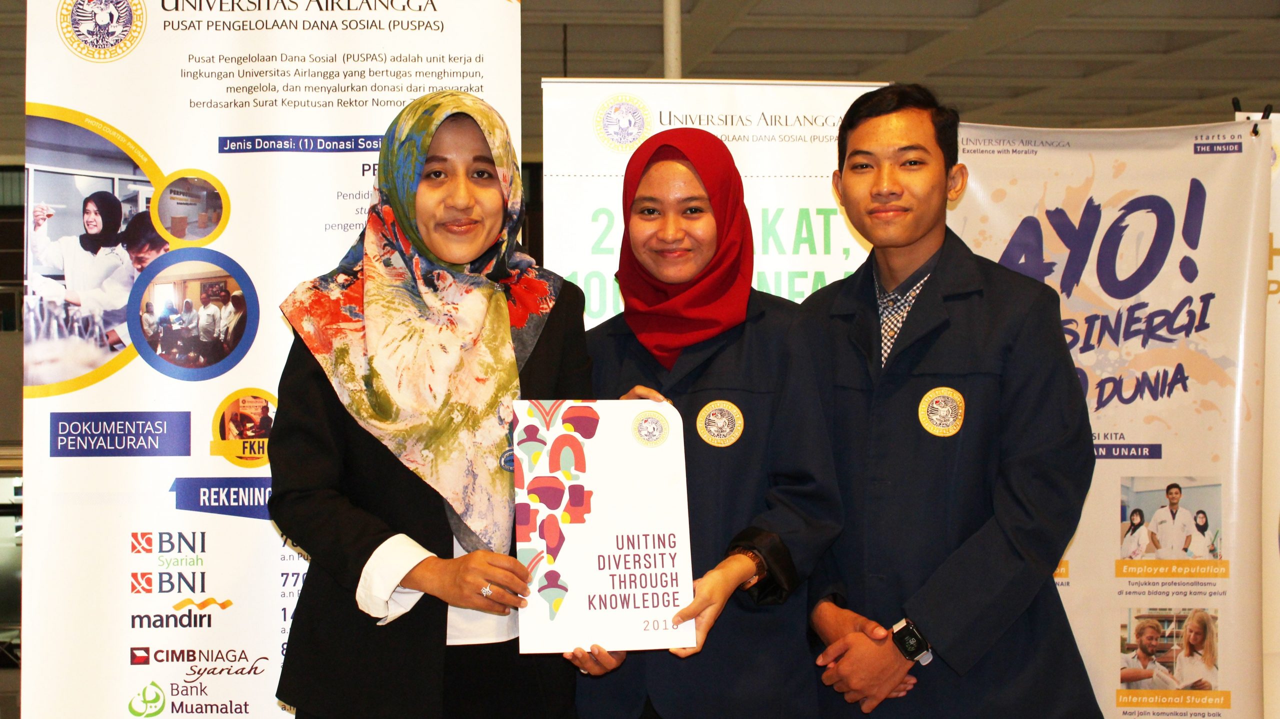 KIRI, Ketua PUSPAS UNAIR Dr. Tika Widiastuti, SE., M.Si., saat menyerahkan bantuan kepada Ketua Tim Ardina Nadya Wahyuhermanto dan Achmad Ubaidillah Mughni untuk mengikuti kompetisi inovasi di Taiwan. (Foto: Alifian Suksma)