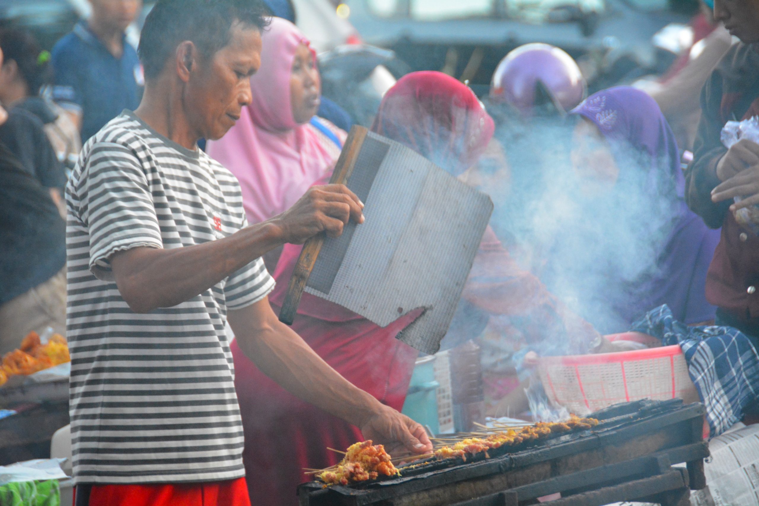 SEORANG pedagang sate sedang mengebaskan kipas di tengah kerumunan pembeli di Street Food Karangmenjangan dekat Kampus B UNAIR. (Foto: Fariz Ilham Rosyidi)