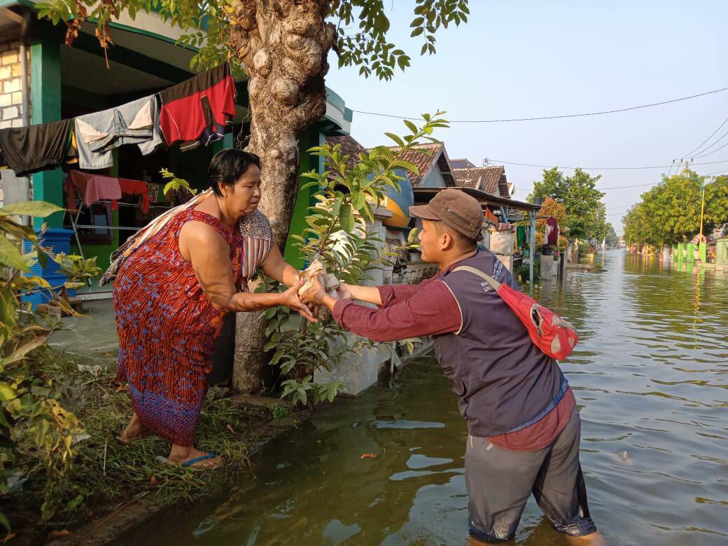 BANJIR setinggi lutut orang dewasa tak menghalangi Tirta Muhammad Rizki, Perwakilan Mahagana UNAIR membagikan logistik ke korban terdampak banjir Gresik (5/5/2019). (Foto: Anastasya Erika Pradani)