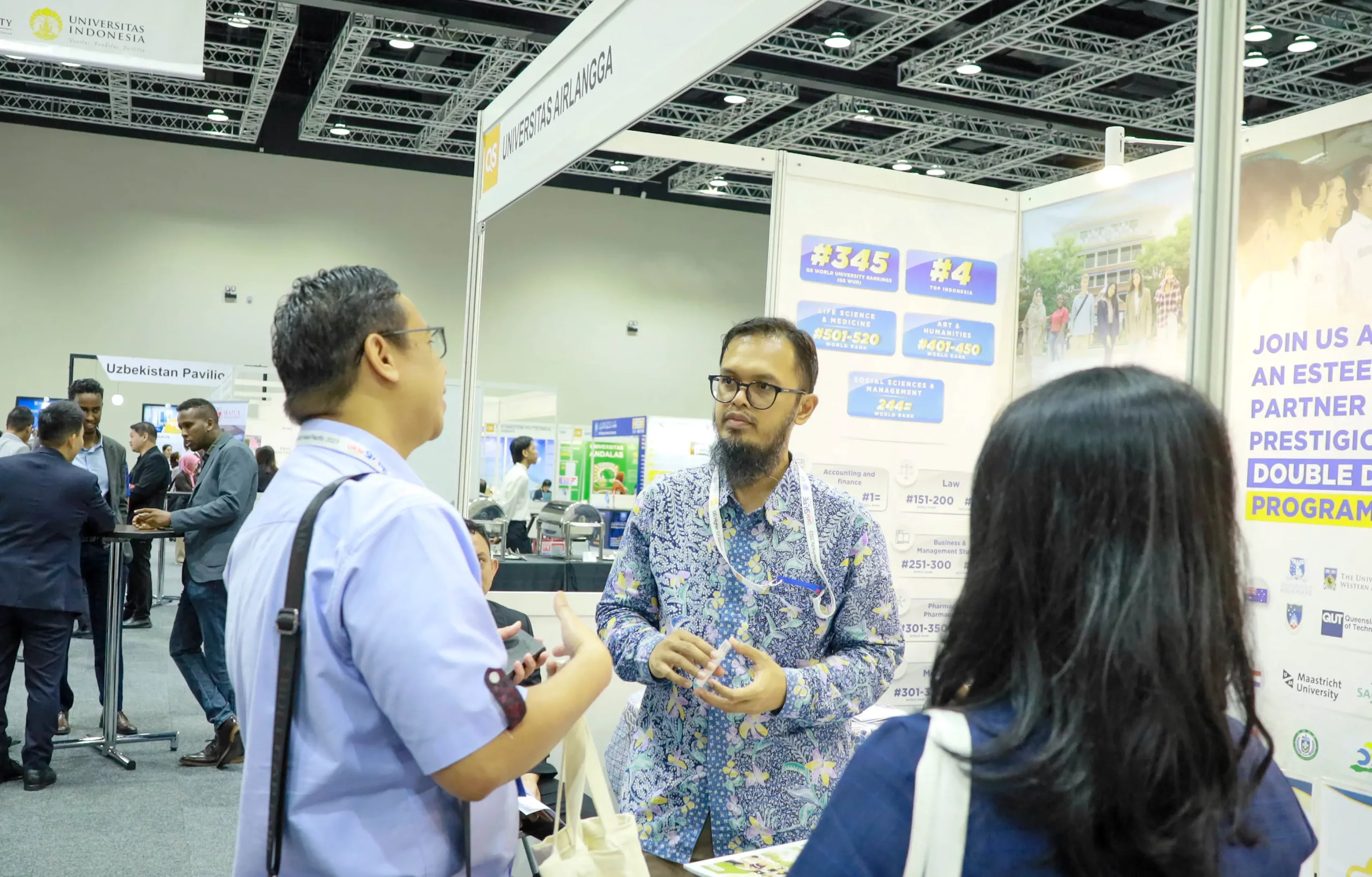 Prof Iman menyambut pengunjung booth UNAIR di QS APAC 2023.