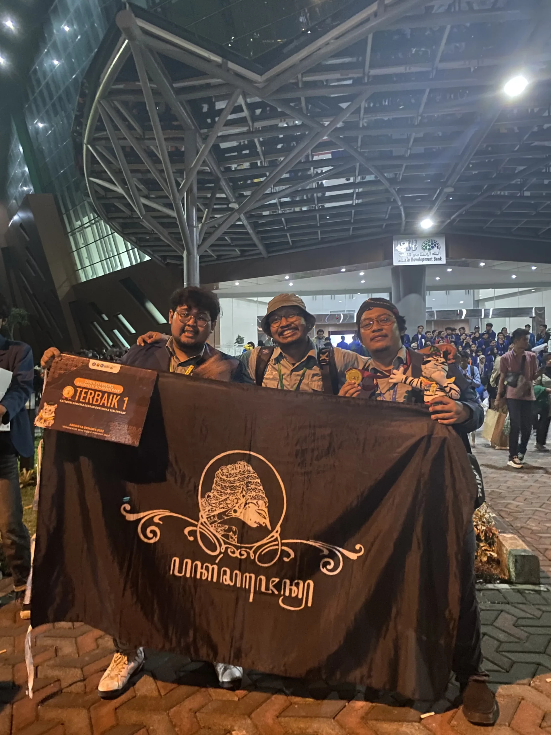 Ketua Ormawa BSO Pakat Sajen (kiri), Dosen Pembimbing (tengah), dan Ketua Pelaksana kegiatan (kanan) berfoto bersama sambil memegang medali dan penghargaan. (Foto: Istimewa)