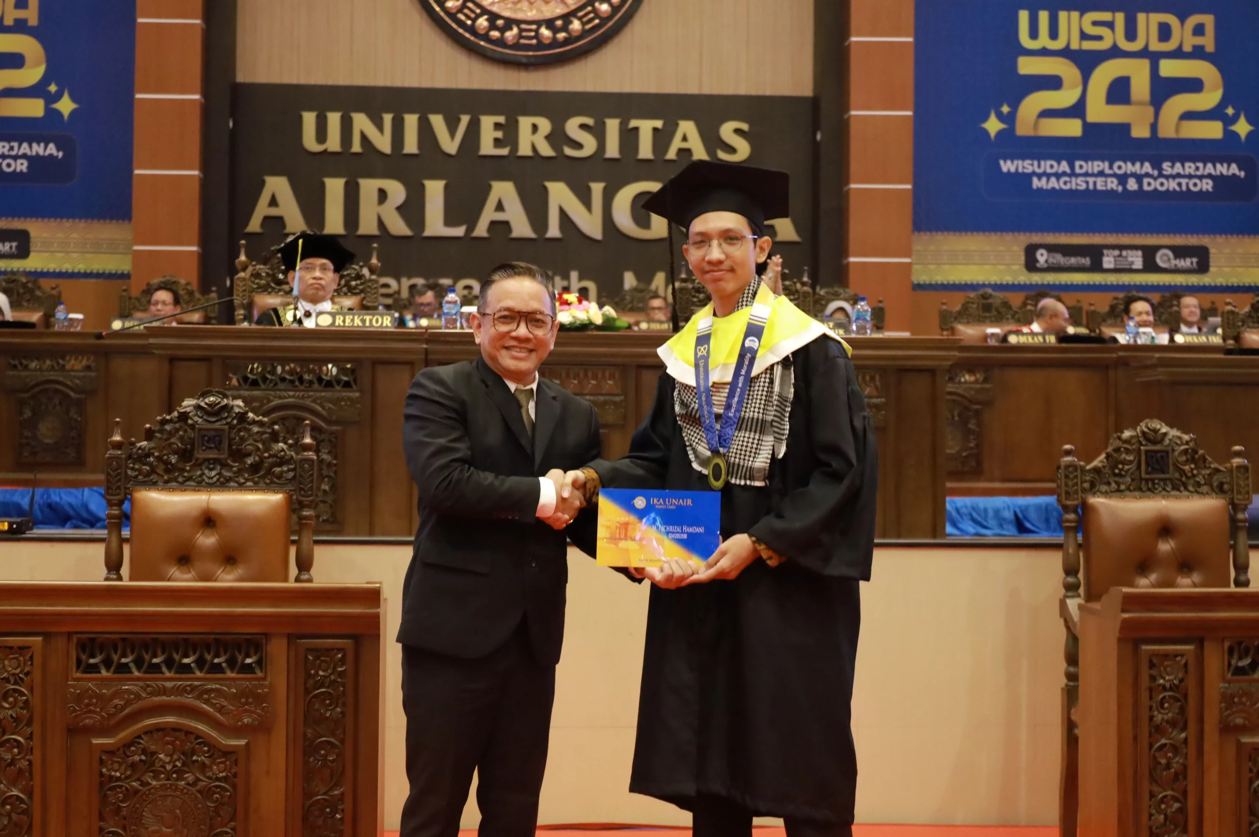 Kiri, Dendi Gustinandar SE M Mn, perwakilan PP IKA UNAIR, memberikan kartu IKA UNAIR kepada Muhammad Fachrizal Hamdani, perwakilan mahasiswa, dalam wisuda ke-242 pada Sabtu (15/06/2024). (Foto: PKIP UNAIR)