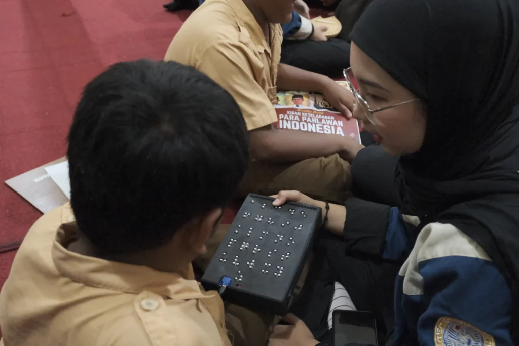 Mahasiswa Teknik Industri UNAIR memperkenalkan Braille Audio Book pada siswa penyandang tuna netra. (Foto: Tim Pengmas).