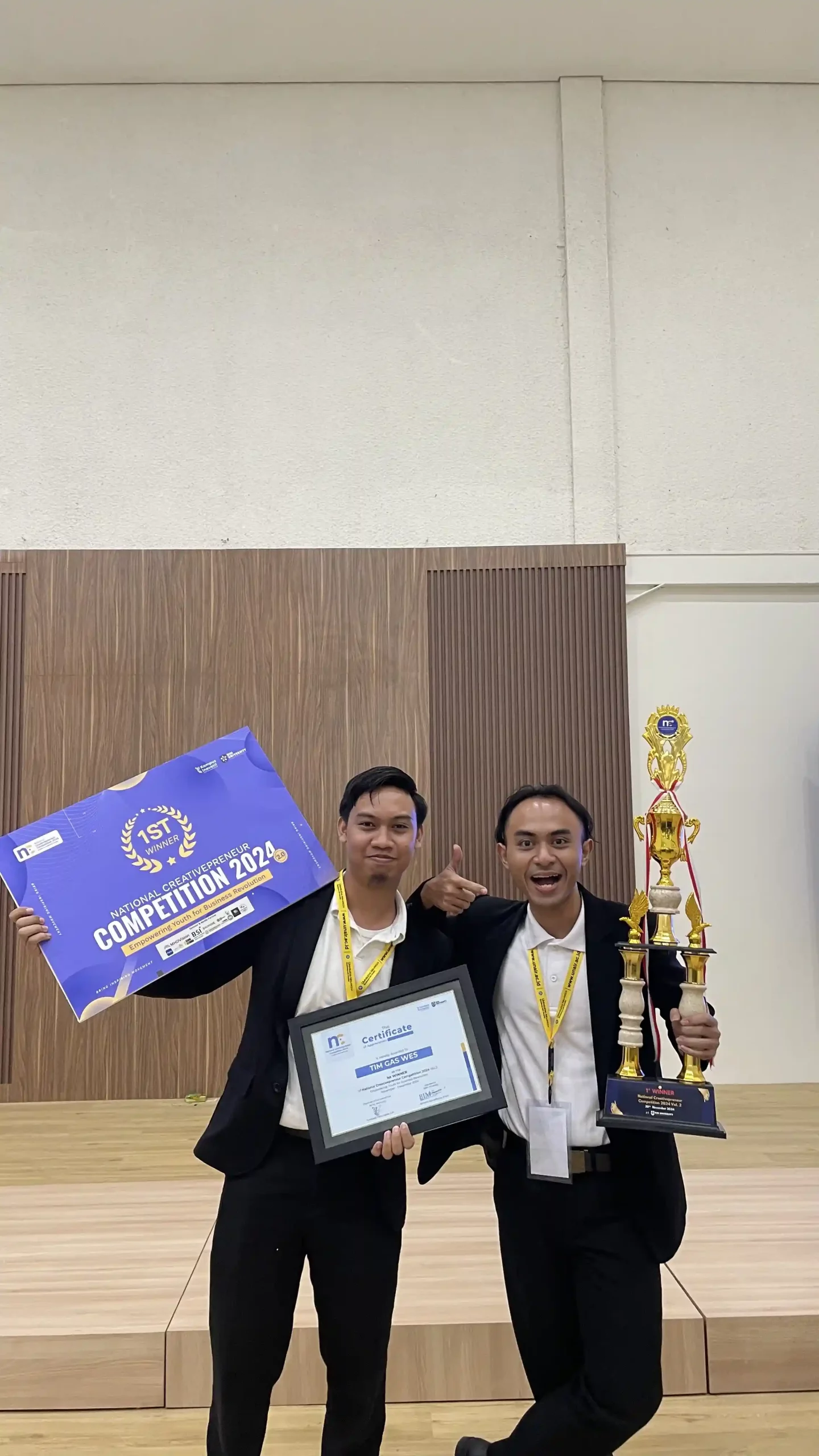 Two students proudly display a plaque in front of a screen after their victory.