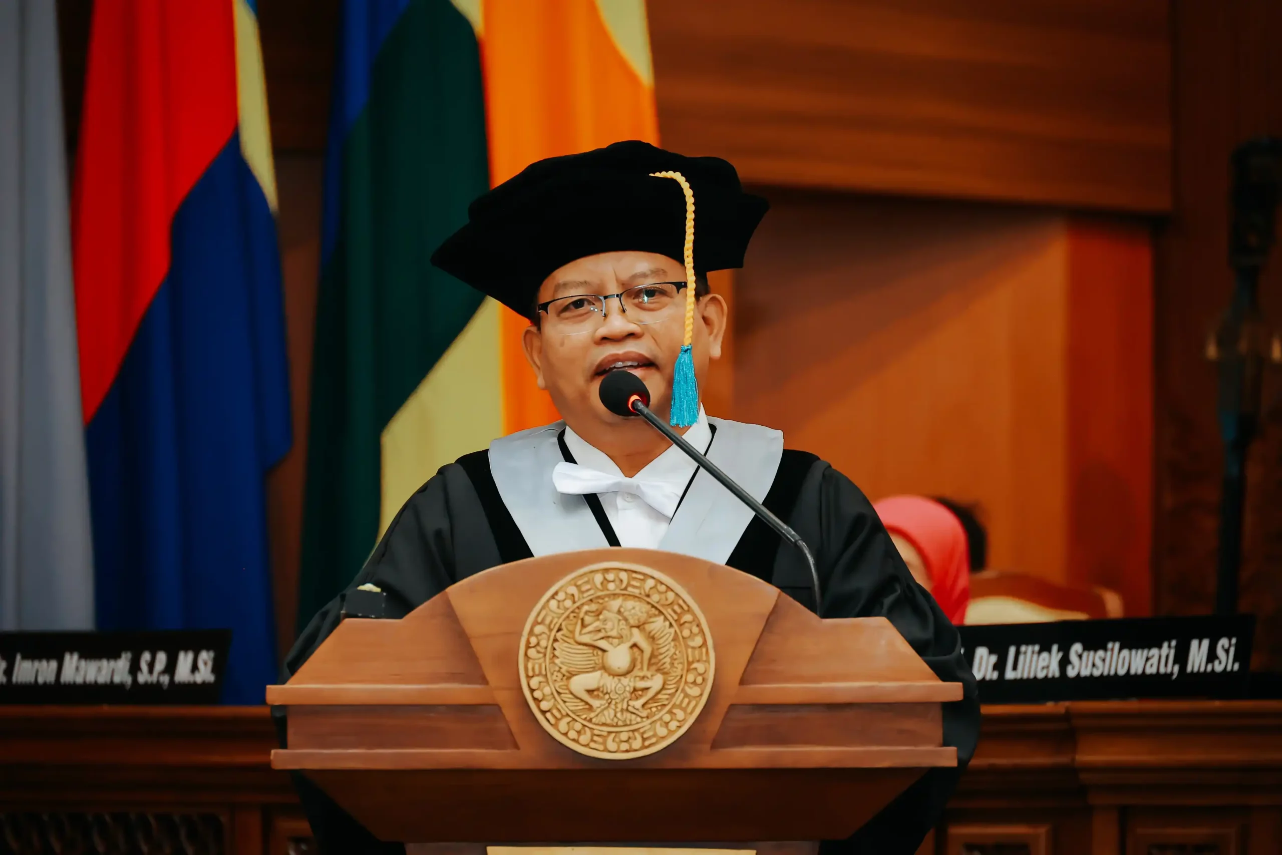 Seorang pria mengenakan toga dan topi wisuda memberikan pidato di depan rektor dan jajaran Universitas Airlangga.