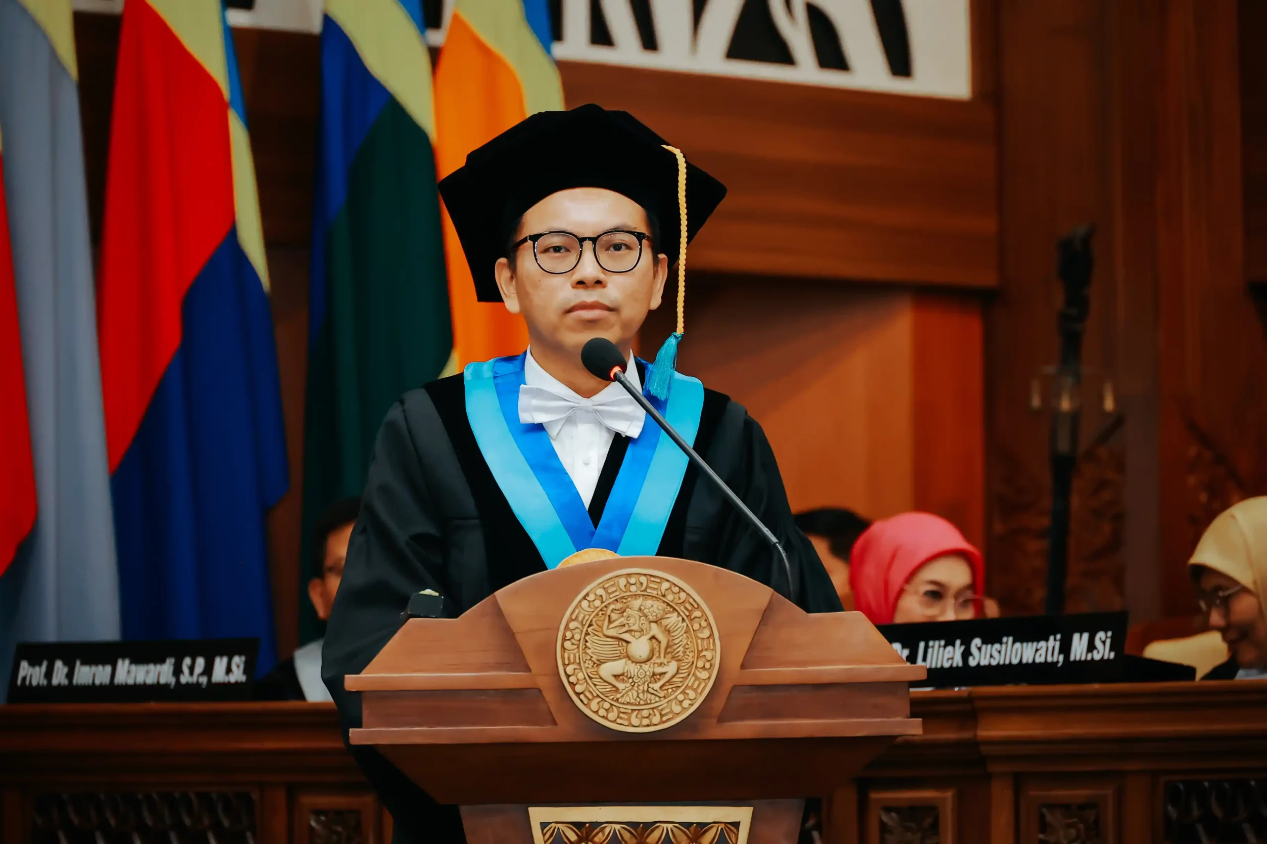 Prof. Efendi in academic regalia stands at a podium during a full professorship conferment ceremony.