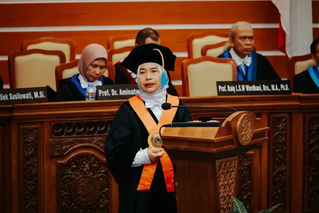 Seorang wanita mengenakan toga berdiri di podium saat pengukuhan guru besar.
