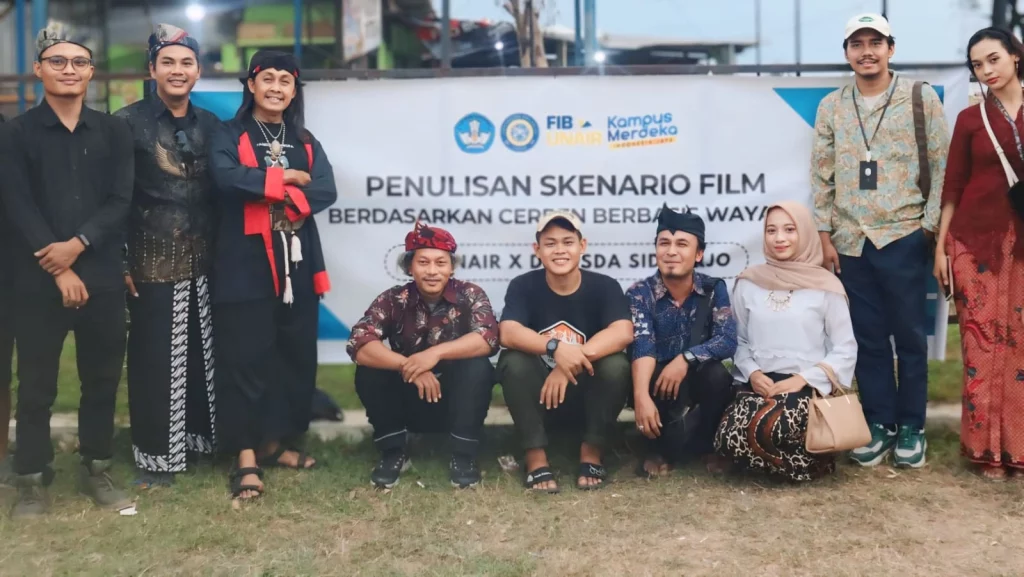 Foto bersama peserta di depan banner acara. empat orang berjongkok dan ada lima orang berdiri