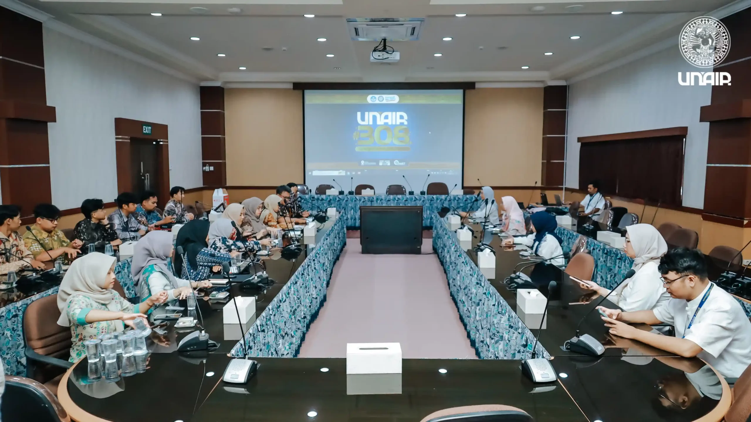 Ruang konferensi dengan peserta yang duduk di meja, terlibat dalam diskusi dan kolaborasi
