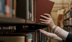Suasana perpustakaan, dua orang sedang mengambil buku dari rak