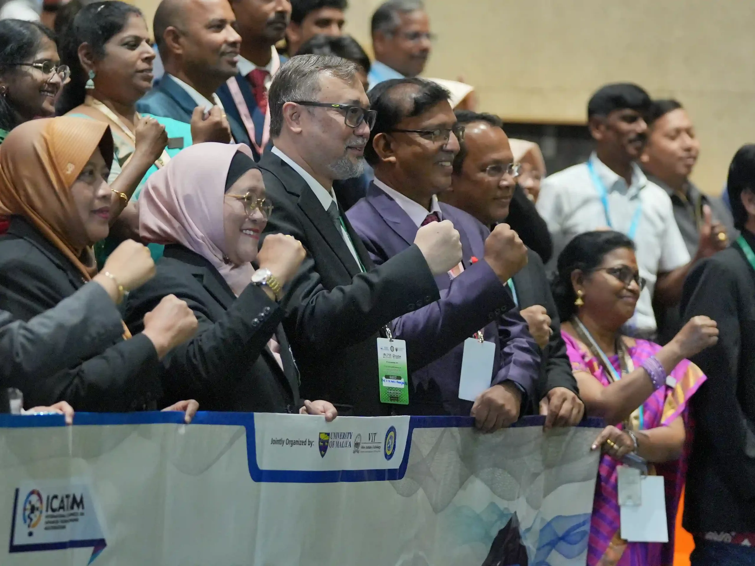 A diverse group of participants pose in formal attire, raising their fists as a gesture of unity and solidarity.