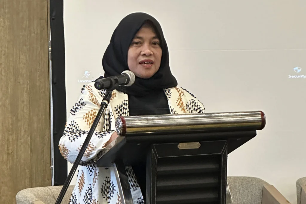 A woman in a black hijab stands at a podium, delivering remarks to an audience.