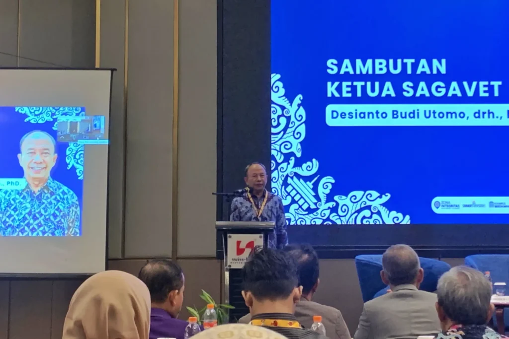 Seorang pria mengenakan baju batik berdiri di podium dengan latar belakang bertuliskan 'Sambutan Ketua SAGAVET Desianto Budi Utomo drh)