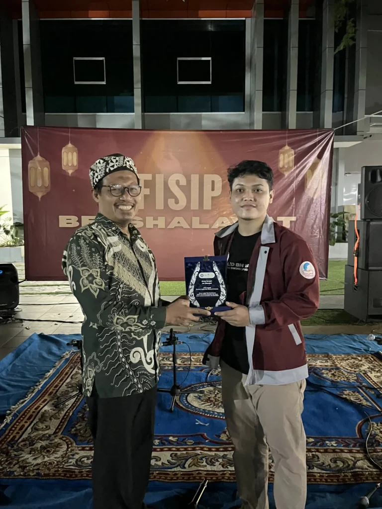 Dekan FISIP UNAIR, M. Muttaqien, S.IP., M.A., Ph.D., menerima plakat penghargaan dari perwakilan panitia “FISIP Bershalawat” sebagai bentuk apresiasi atas dukungannya dalam kegiatan Hari Santri Nasional 2025 di lingkungan FISIP UNAIR. (Dokumentasi: Panitia)