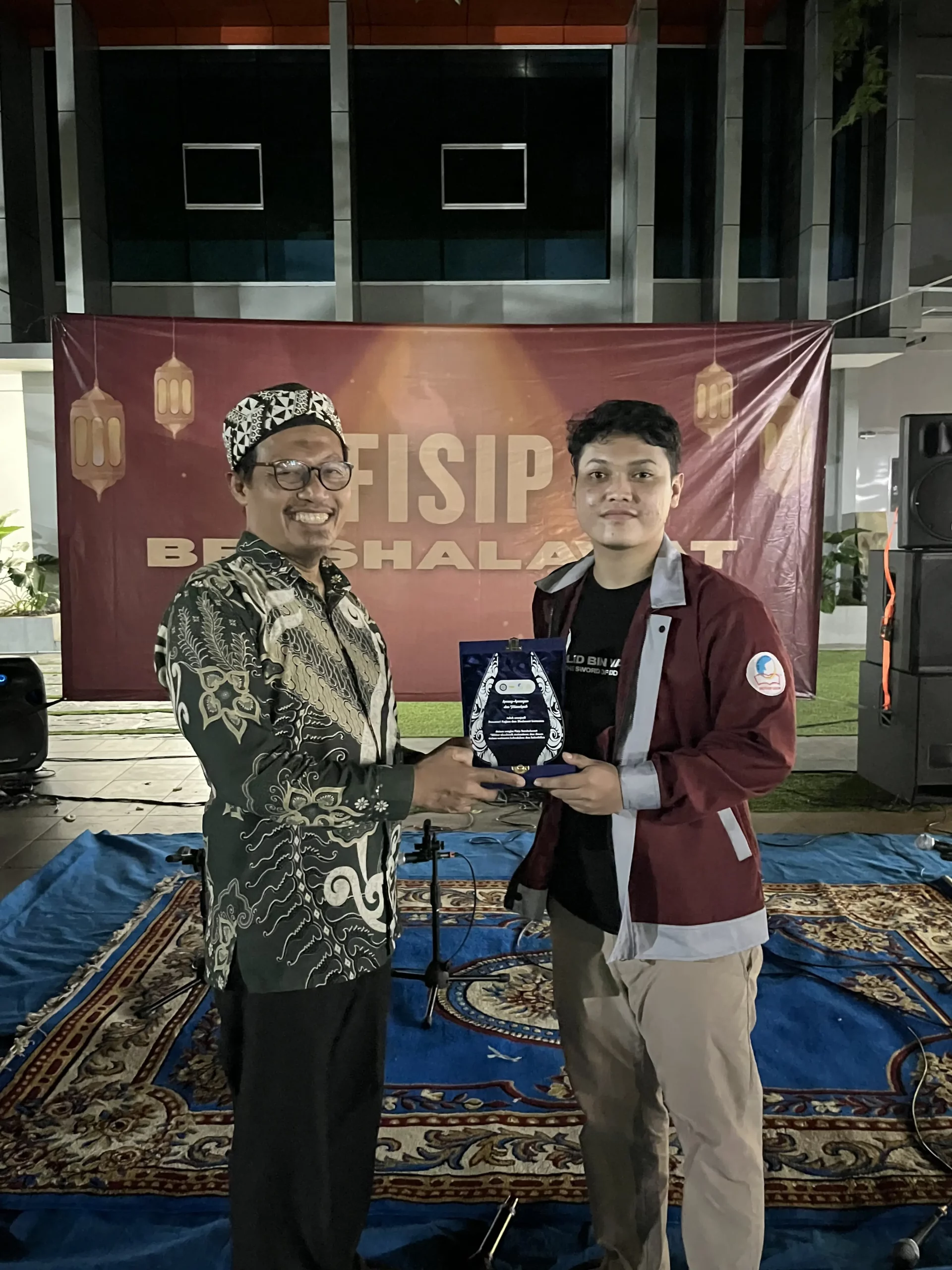 Dekan FISIP UNAIR, M. Muttaqien, S.IP., M.A., Ph.D., menerima plakat penghargaan dari perwakilan panitia “FISIP Bershalawat” sebagai bentuk apresiasi atas dukungannya dalam kegiatan Hari Santri Nasional 2025 di lingkungan FISIP UNAIR. (Dokumentasi: Panitia)