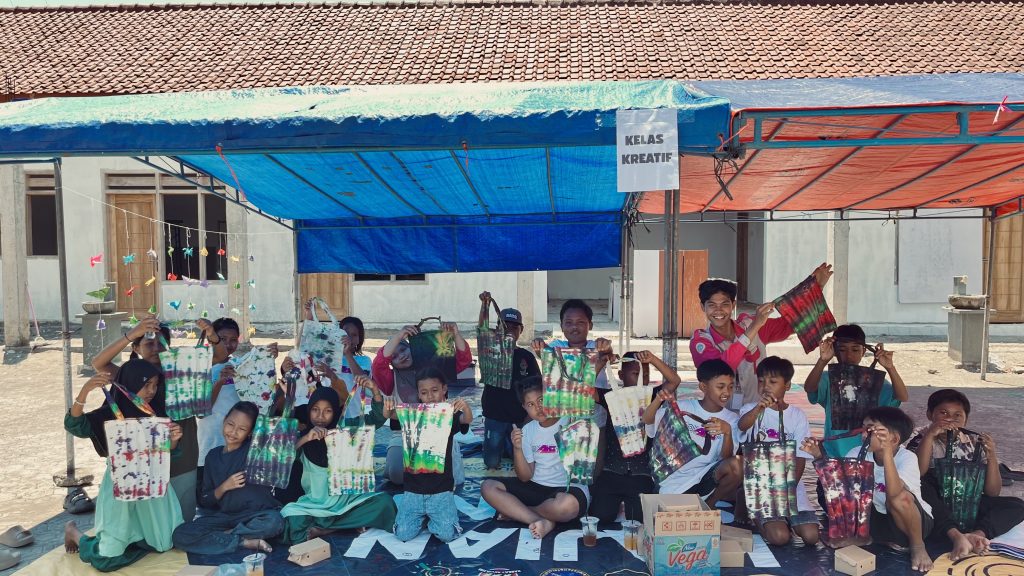 Potret tim PPK Ormawa SEJATI bersama siswa-siswi SDN 04 Kendalrejo saat memperlihatkan hasil karya tie dye mereka dengan penuh antusias. (Foto: istimewa).