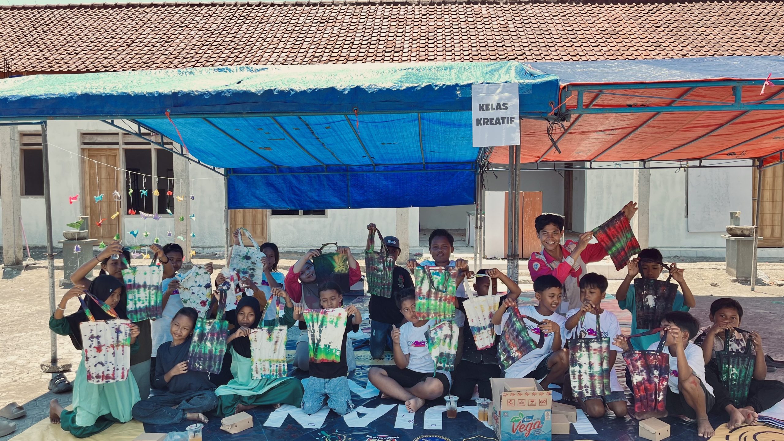 Potret tim PPK Ormawa SEJATI bersama siswa-siswi SDN 04 Kendalrejo saat memperlihatkan hasil karya tie dye mereka dengan penuh antusias. (Foto: istimewa).