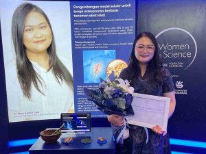 A woman stands holding a certificate and bouquet, she is Dr. Maria Apriliani Gani, an alumna of UNAIR’s PMDSU program.