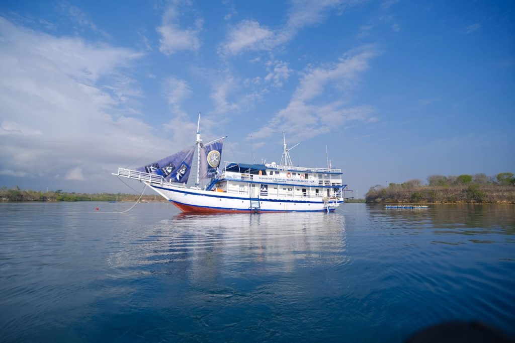 Sebuah kapal dengan warna dominan putih dan biru berlayar di tengah lautan