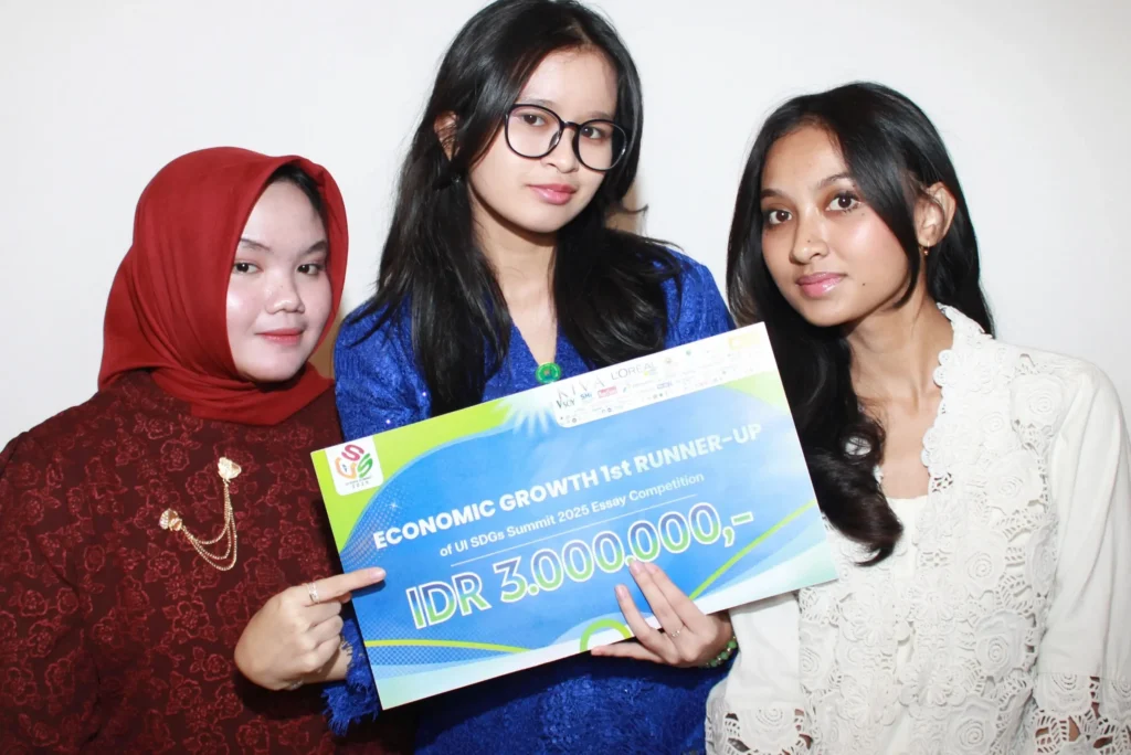 Three female university students pose while holding an award plaque that reads “Economic Growth 1st Runner-Up – UI SDGs Summit 2025 Essay Competition,” with a prize of IDR 3,000,000. They stand in front of a plain background and smile at the camera.