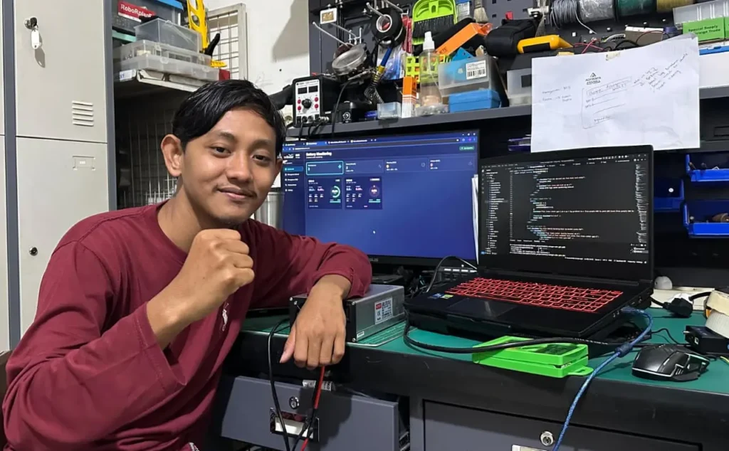 A picture of a man next to his personal computer named Moch Ihwanul Abidin Dwi Tama, alumnus of the Robotics Engineering and Artificial Intelligence program at Faculty of Advanced Technology and Multidiscipline (FTMM), Universitas Airlangga