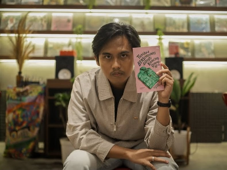 A man poses with a book titled “Tuhan Bersembunyi Seperti Kancing Cadangan.”