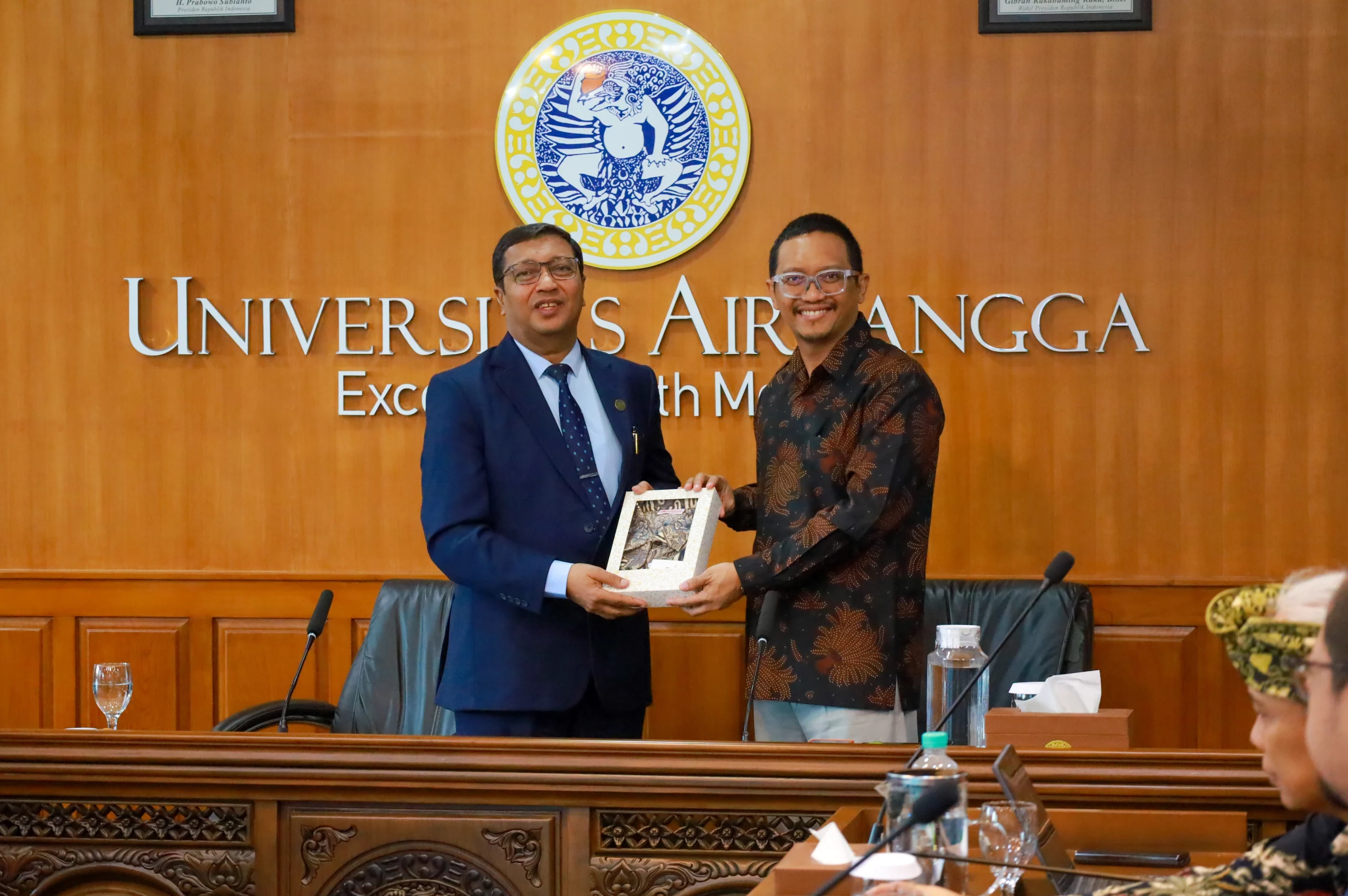 Seorang laki-laki berjas biru menerima cinderamata dari wakil rektor UNAIR