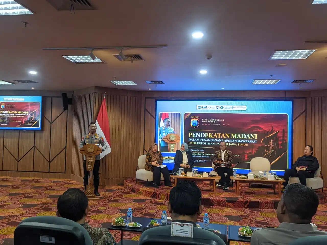 Kombes. Pol. Dr. Luthfi Sulistiawan menyampaikan sambutannya (sebelah kiri) beserta tiga narasumber lainnya (sebelah kanan) pada seminar nasional bertajuk pendekatan madani dalam penanganan laporan masyarakat oleh kepolisian daerah Jawa Timur. (Foto: Ainnur Ayu Nanda Agustin)