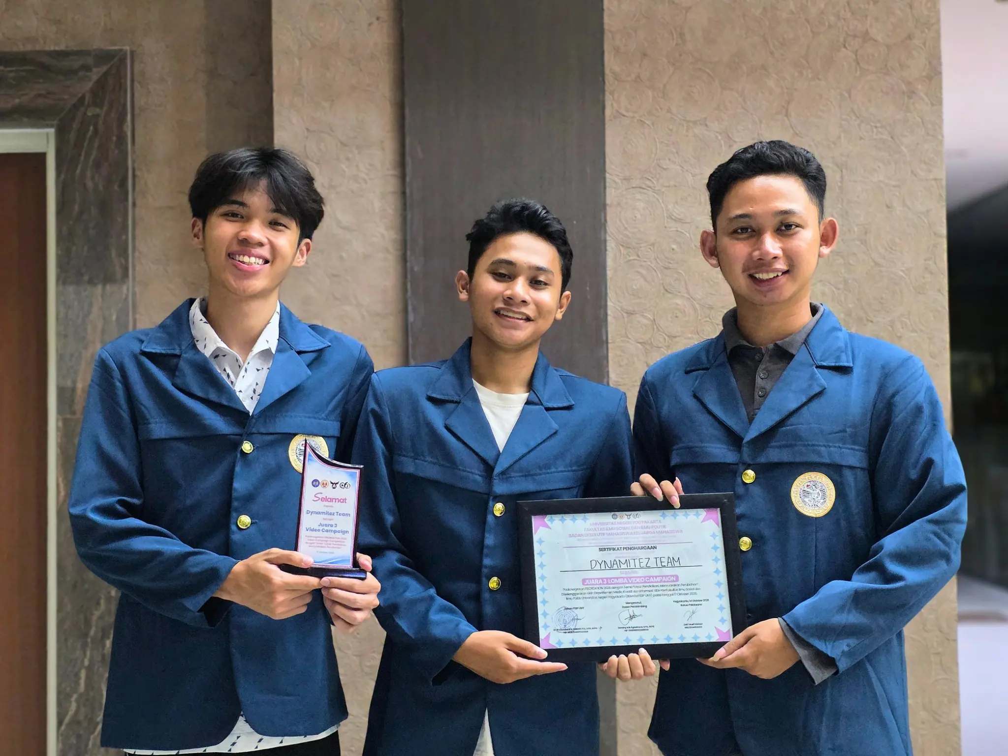 Tim Dynamitez, beranggotakan tiga mahasiswa UNAIR, menunjukkan piala dan sertifikat penghargaan Juara 3 Lomba Video Campaign FISCREATION 2026. Piala dan sertifikat itu mereka terima dari BEM KM FISIP Universitas Negeri Yogyakarta. (Foto: Dokumentasi pribadi Muhammad Razif Arsyad)