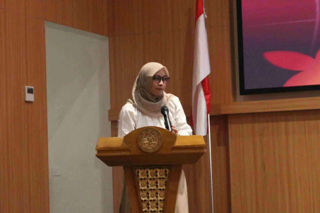 Seorang perempuan mengenakan baju putih dan jilbab krem berdiri di atas podium. Ia adalah Dr Ratri Maya Sitalaksmi drg MKes PhD SpPros(K) saat menjelaskan regulasi Mawapres UNAIR 2027