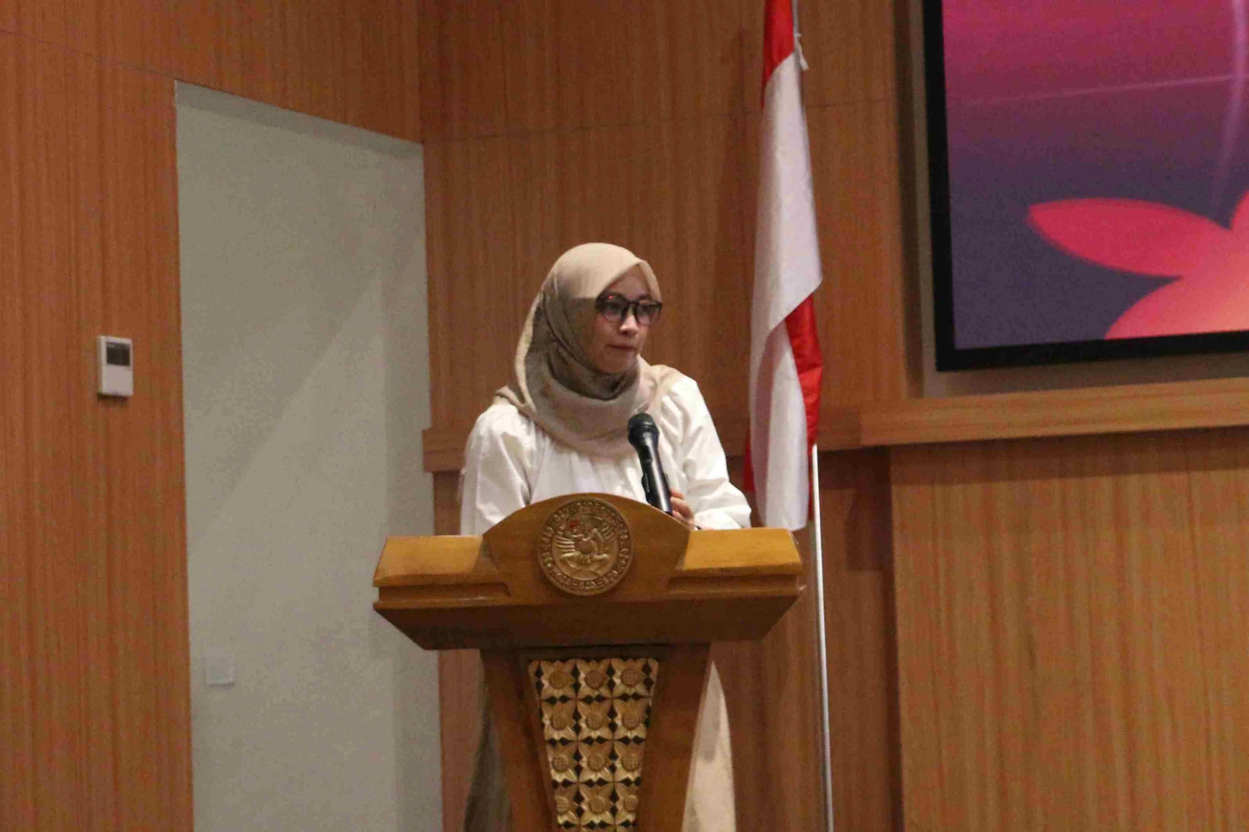 Seorang perempuan mengenakan baju putih dan jilbab krem berdiri di atas podium. Ia adalah Dr Ratri Maya Sitalaksmi drg MKes PhD SpPros(K) saat menjelaskan regulasi Mawapres UNAIR 2027